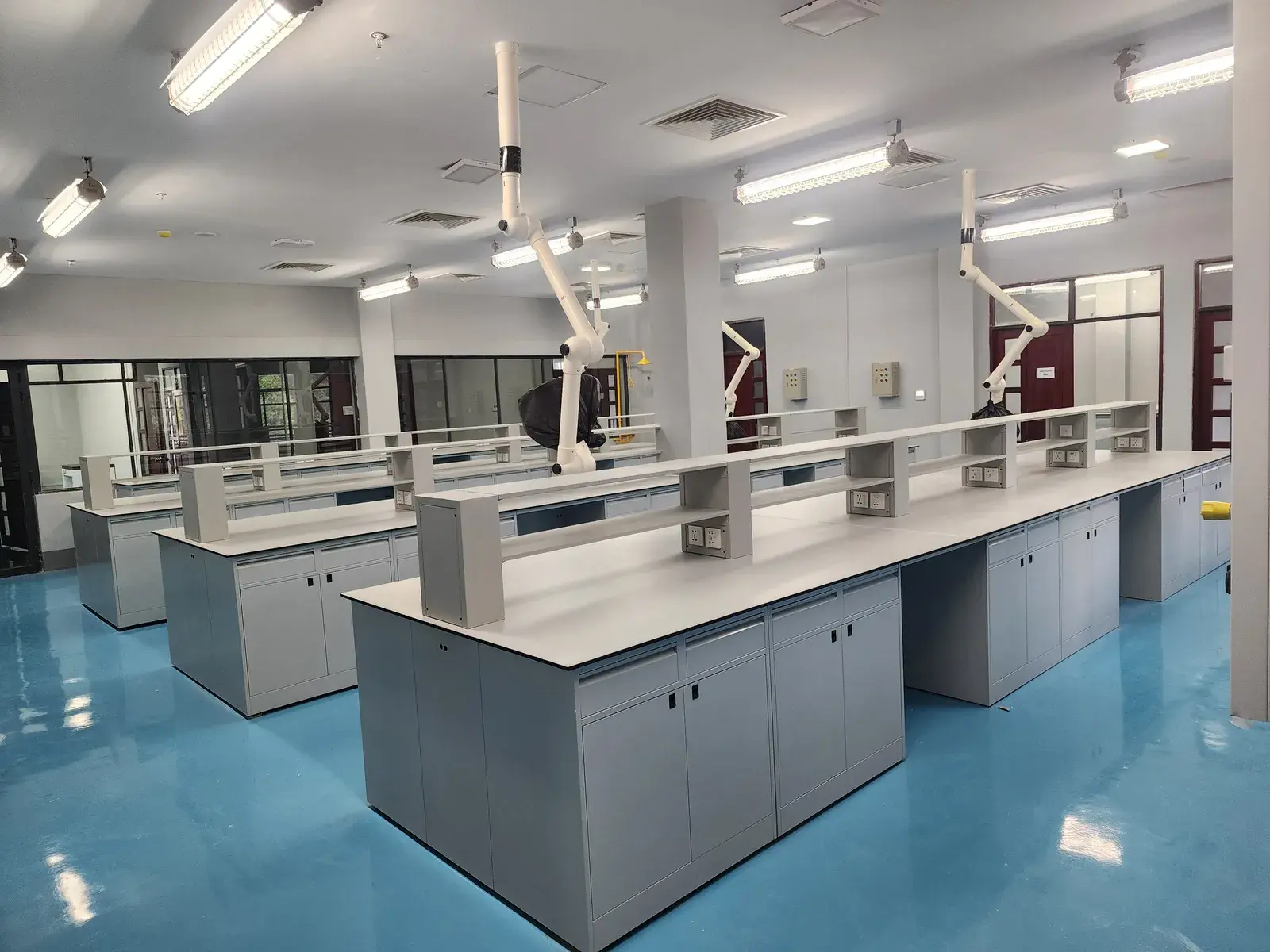 The completed laboratory — island benches with reagent shelving and ceiling-mounted extraction arms