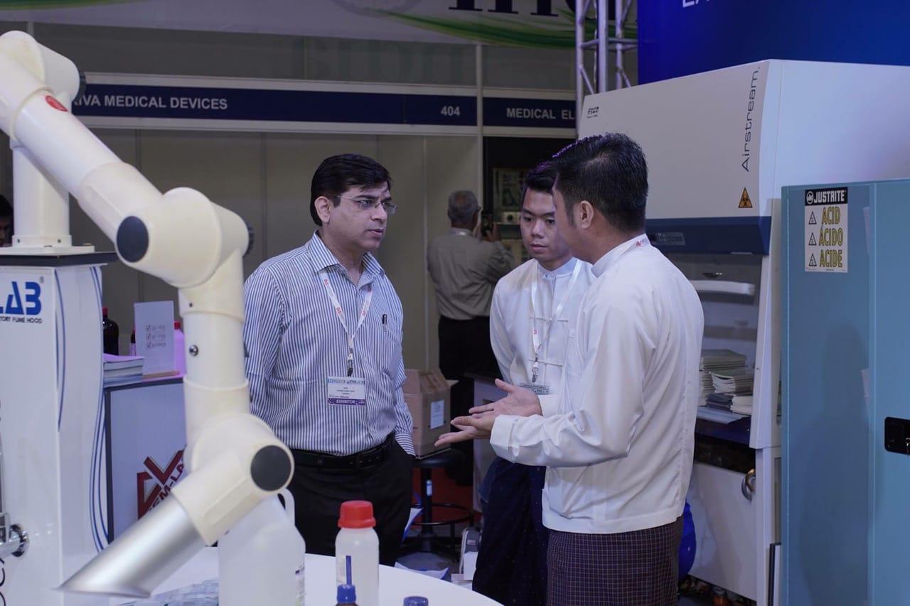 FIRST PRIME staff explaining the fume hood and robotic arm setup to a visiting exhibitor