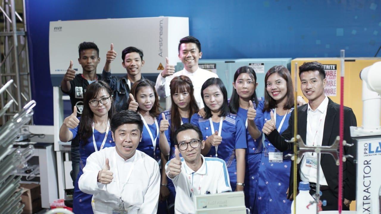 Wide group photo of the FIRST PRIME exhibition team giving a thumbs-up